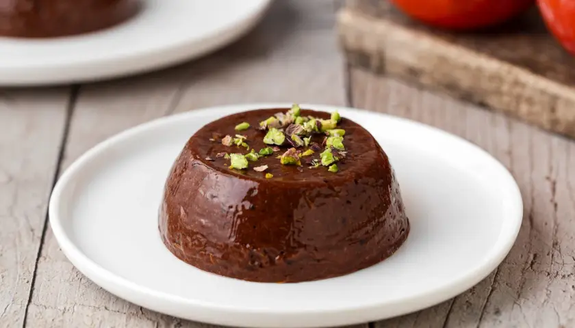 Budino di cachi al cioccolato, guarnito con pistacchi tritati, servito su un piatto bianco.