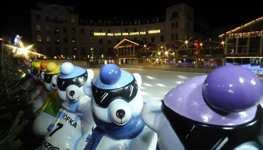 Bunte Eisbären-Figuren am Stachus Weihnachtsmarkt in München, mit Lichtern und einer Eisbahn im Hintergrund.
