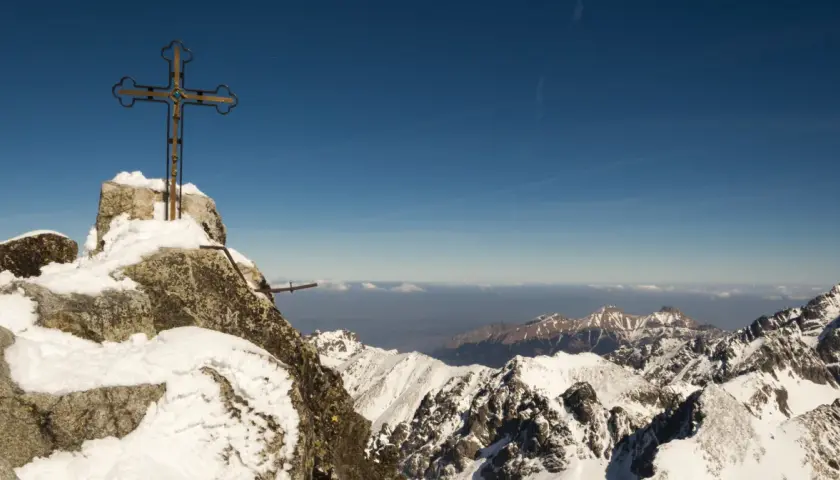 Krzyż na szczycie Gerlach, pokryty śniegiem. Widok na ośnieżone Tatry. Uważaj, by nie dostać mandatu za wejście na Gerlach bez przewodnika!