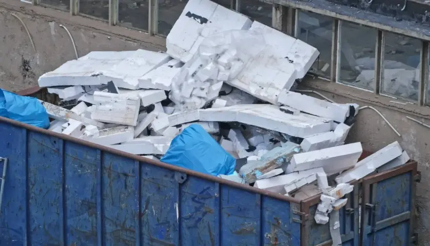 Kontener z niebieskimi workami i pociętym styropianem.