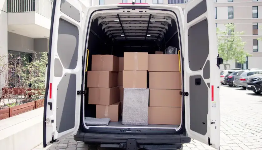 Ein weißer Transporter mit geöffneten Hecktüren, beladen mit vielen braunen Paketen. Was ist ein Transporter? Ein Fahrzeug für Lieferungen.