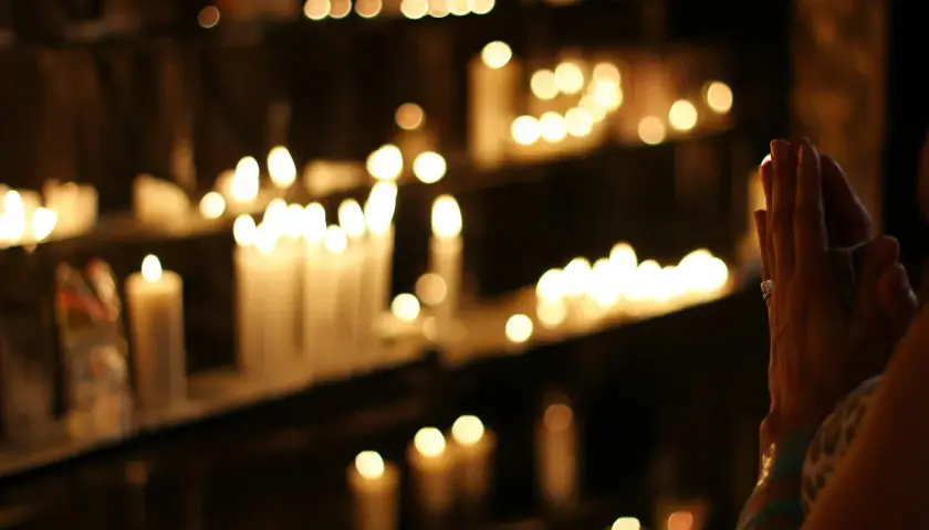 Dłonie złożone do modlitwy wieczornej do Matki Bożej, w blasku zapalonych świec.
