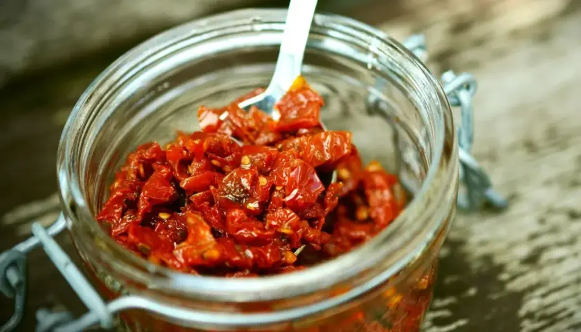 Słoik pełen aromatycznej pasty z suszonych pomidorów, gotowej do użycia. Łyżeczka zanurzona w czerwonej masie.