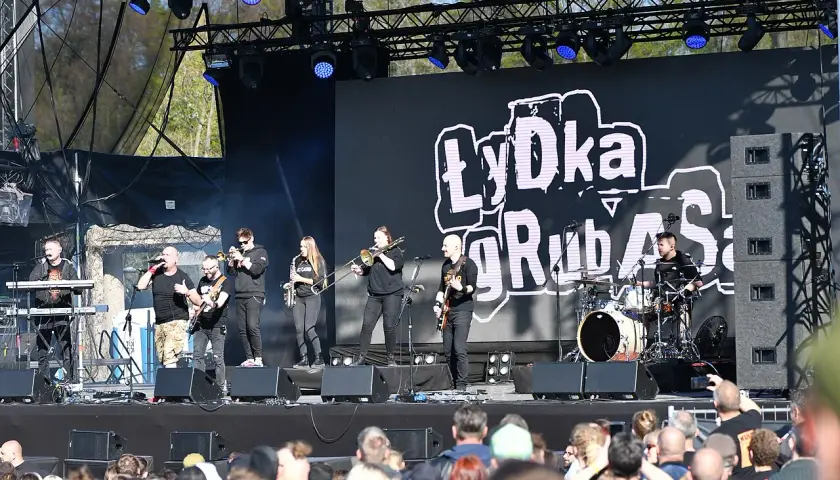 Zespół Łydka Grubasa na scenie, grający koncert. W tle wielki ekran z logo zespołu.
