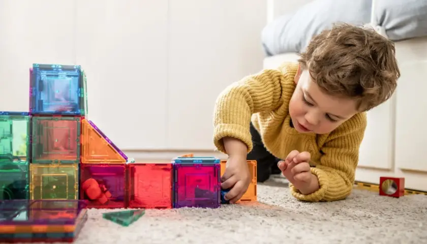 Niño concentrado jugando con bloques magnéticos de colores, ideales para actividades para niños de 2 a 3 años.