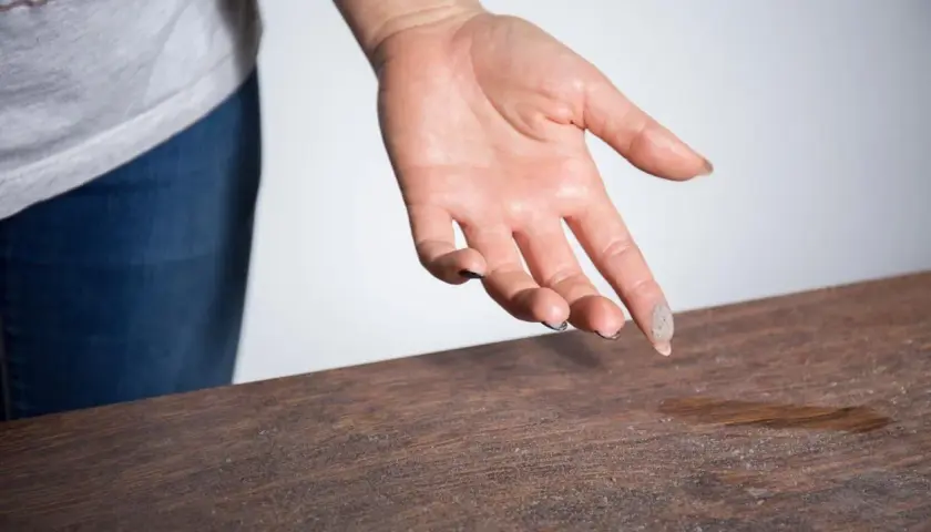 Mano con polvo en los dedos sobre una mesa de madera. Una demostración visual de cómo eliminar el polvo del aire y las superficies.