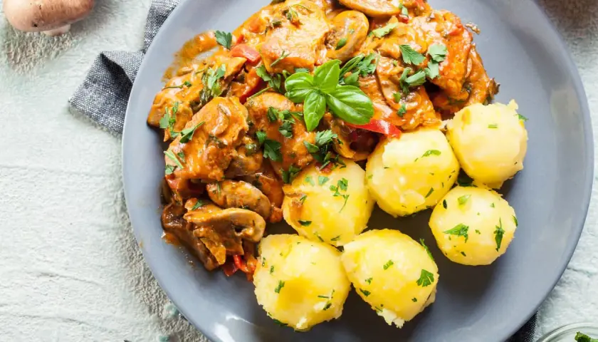 Pyszny gulasz z indyka w sosie z pieczarkami i papryką, podany z kluskami śląskimi posypanymi natką pietruszki.