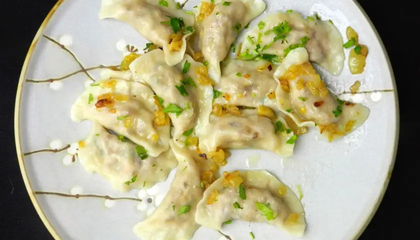 Pyszne pierogi z kaszą gryczaną bez sera, okraszone cebulką i posypane natką pietruszki.