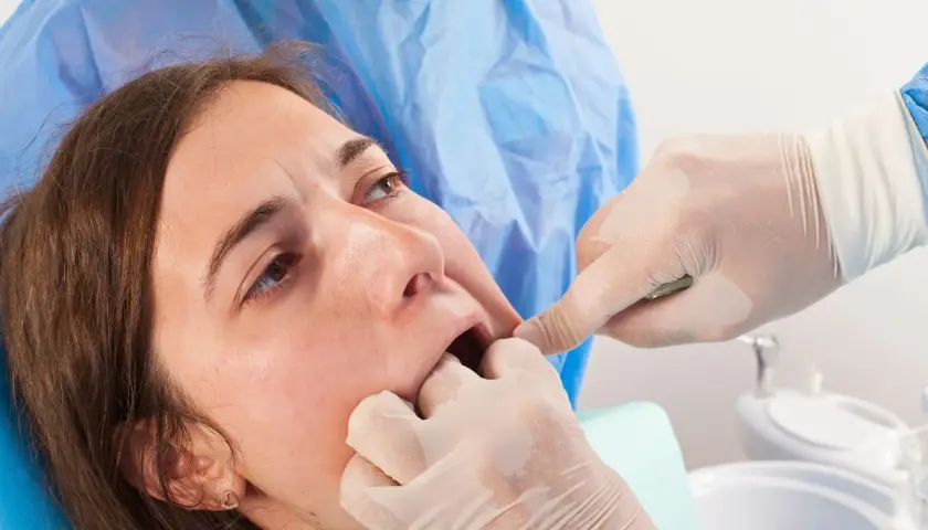 Dentista examina la boca de una paciente, notando un posible coagulo muela blanco.