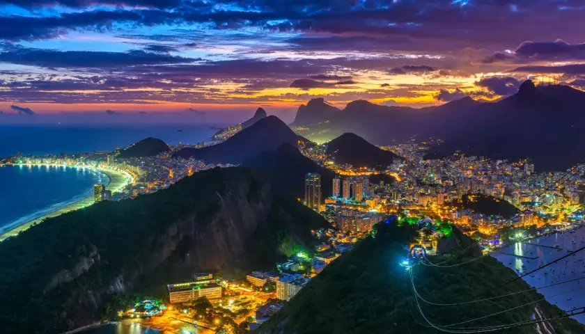 Rio de Janeiro bei Dämmerung: Lichter der Stadt, der Strand und die Berge unter einem dramatischen Himmel.