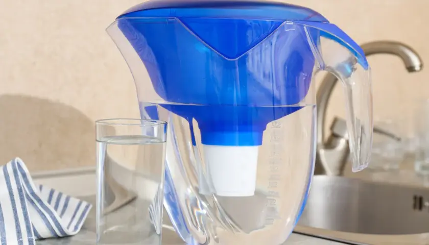 Dzbanek filtrujący wodę, szklanka czystej wody i ręcznik. Dbanie o czystą wodę to walka z mikroplastikiem w wodzie.