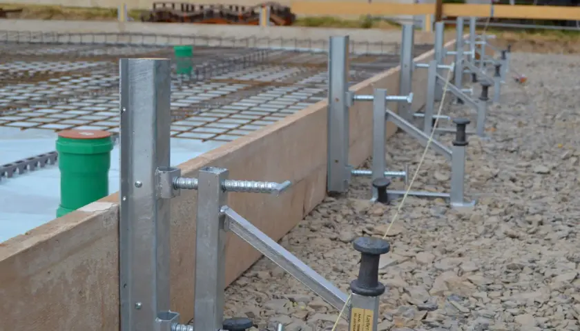Stahlstützen und Holzbretter bilden die schalung wand für eine Betonplatte. Bewehrungsstahl und grüne Rohre sind sichtbar.