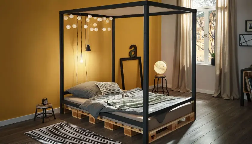 Ein modernes Himmelbett, das man leicht selber bauen kann, mit Paletten als Basis. Lichterketten und eine gelbe Wand schaffen Gemütlichkeit.