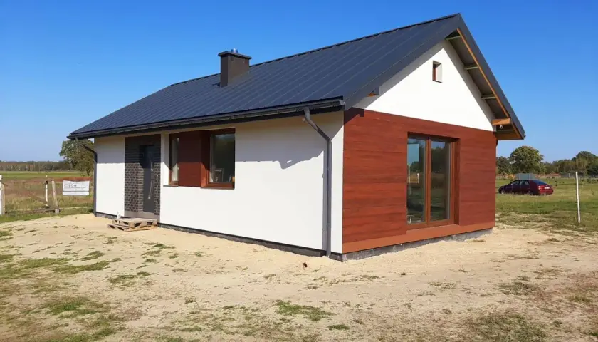 Nowy dom szkieletowy na zgłoszenie, z białym tynkiem i drewnianą elewacją, gotowy do zamieszkania.