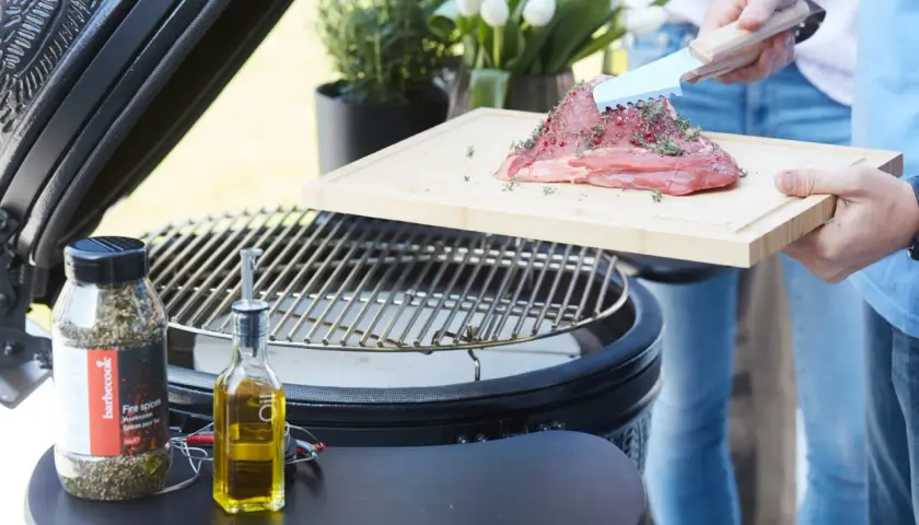 Un morceau de viande **black angus** assaisonné, prêt à être grillé. Huile d'olive et épices à proximité.