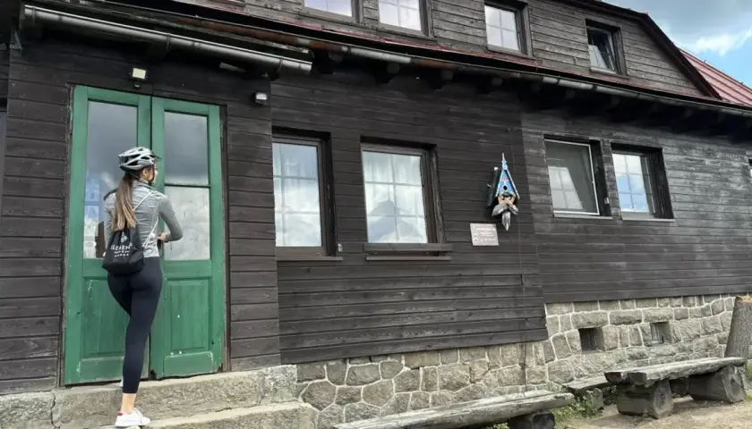 Kobieta w kasku rowerowym zbliża się do drzwi schroniska Chatka Górzystów.