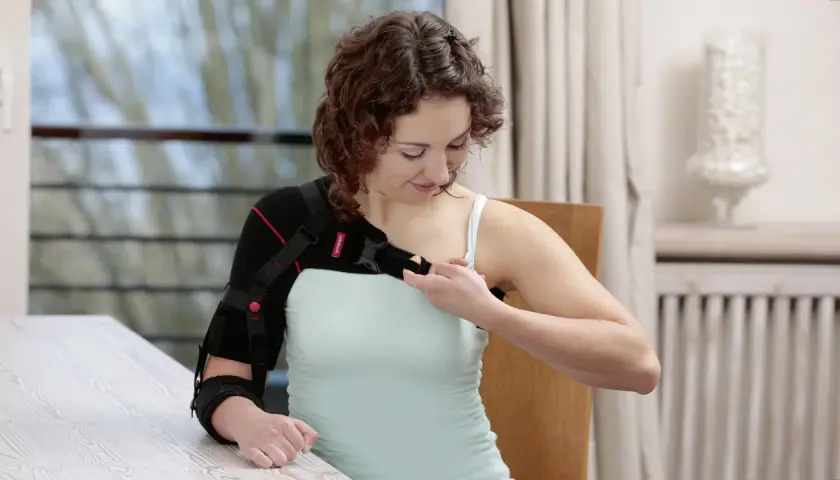 Frau legt sich eine Armorthese an, um ihre Schulter zu stabilisieren.