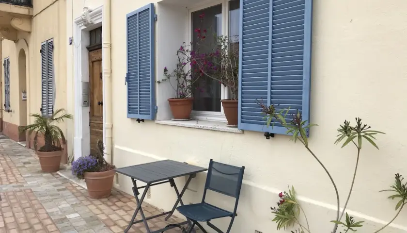 Bonjour! Co to znaczy? Uroczy zakątek z niebieskimi okiennicami, stolikiem i krzesłem, zapraszający do odpoczynku.