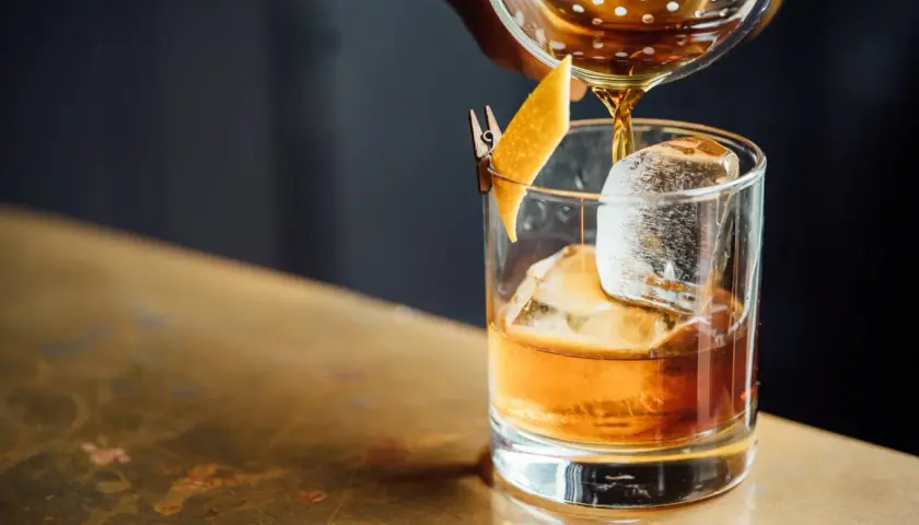 Whisky z colą: profanacja czy dopuszczalny mix? Bursztynowy trunek z lodem i skórką pomarańczy, nalewany ze shakera.