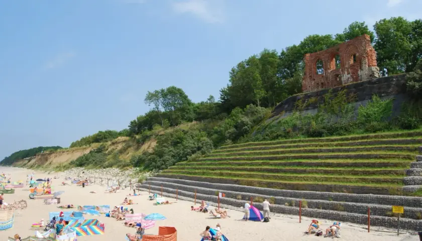 Plaża w Rewalu z ruinami na klifie. Ludzie odpoczywają na piasku, ciesząc się słońcem i widokiem. To popularne rewal atrakcje.