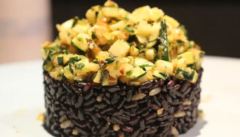 Riso nero compattato a cilindro, guarnito con un'abbondante porzione di zucchine saltate e erbe aromatiche.