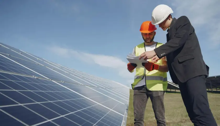 Deux hommes en casque discutent des plans près de panneaux solaires, en vue du remplacement d'un appareil sous garantie.
