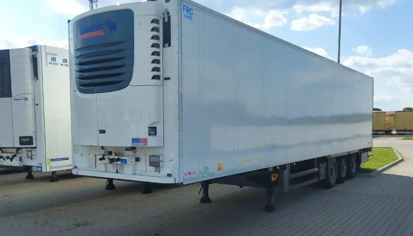Biała naczepa chłodnia Schmitz Cargobull z niebieskim logo, zaparkowana na zewnątrz.