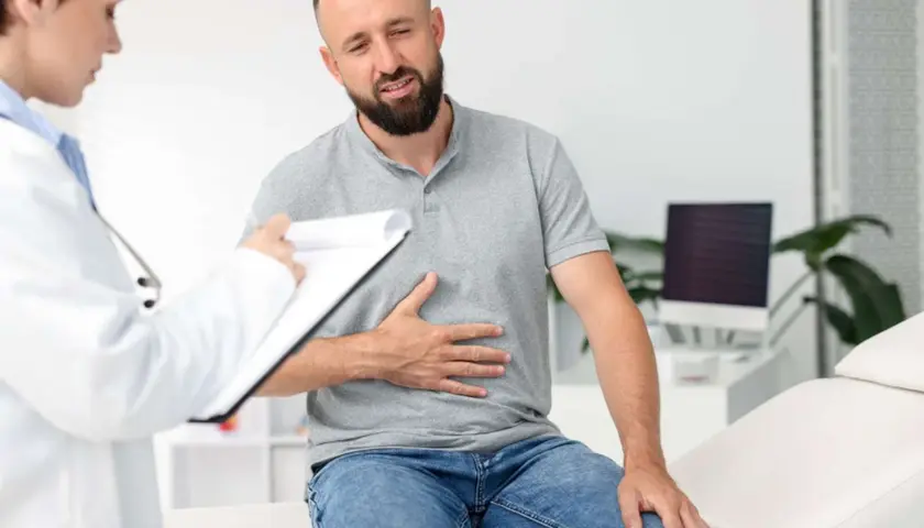 Mężczyzna z bólem brzucha, prawdopodobnie jelitówka, rozmawia z lekarką w gabinecie.