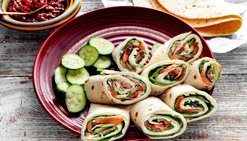 Pyszna tortilla z łososiem, serkiem i świeżym ogórkiem, podana z pikantnym sosem. Idealna na szybki lunch.