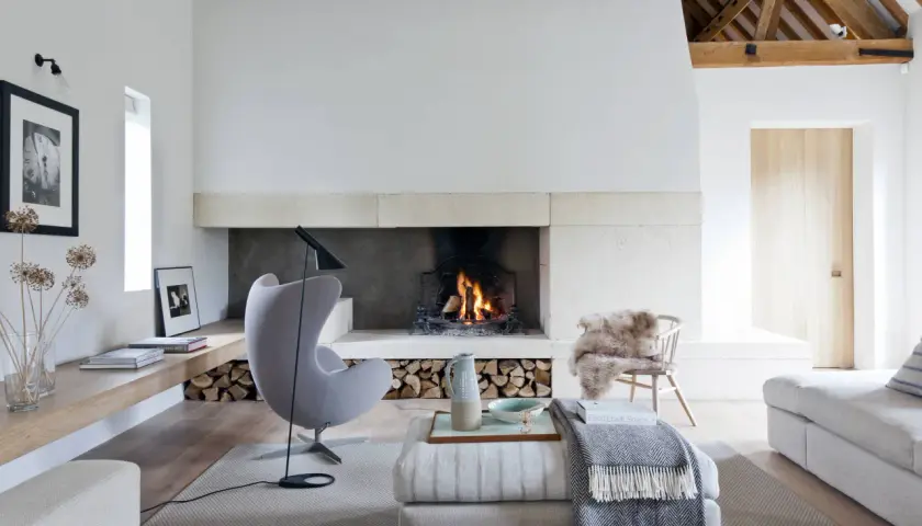 Acogedor salón con un mueble con chimenea encendida, sillón gris, sofás y decoración rústica.
