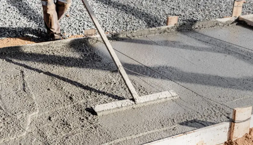 Un ouvrier lisse une **pente en béton** fraîchement coulée avec un râteau, créant une surface lisse pour une nouvelle construction.