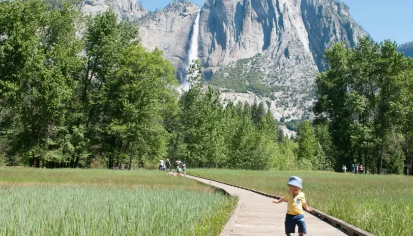 Mały chłopiec na ścieżce w Yosemite, w tle wodospad i trzy korony gór.