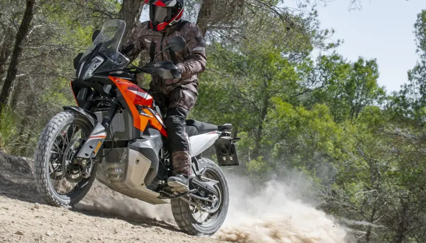 Motociclista con casco y equipo de aventura, derrapando una KTM 490 Adventure en un camino de tierra con polvo levantándose.