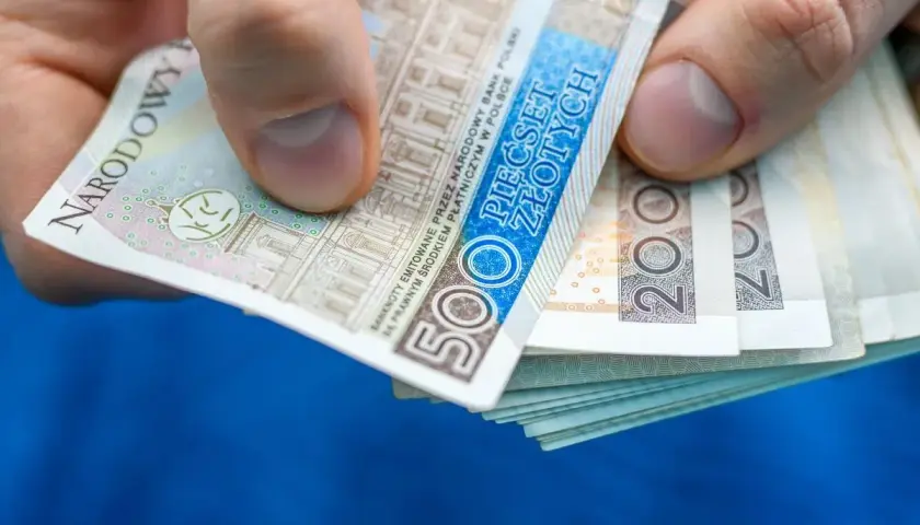 Dłoń trzyma stos banknotów 500 zł i 200 zł. Może to być zapłata za rachunek, np. taryfa urzędowa Energa.