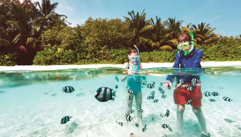 Bambini con maschera e boccaglio nuotano tra pesci colorati in acque cristalline, un'idea perfetta per sapere dove andare in vacanza con i bambini all'estero.