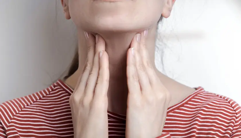 Femme touchant sa gorge, possible symptôme mononucléose. Douleur ou gonflement au cou.