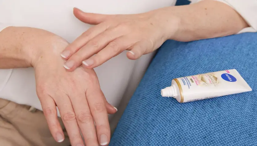 Mani che si applicano crema, forse per alleviare il prurito avambracci cause. Tubetto Nivea in primo piano.