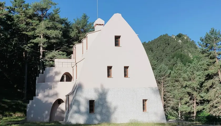 Edificio singular en la Serra de Catllaras, rodeado de pinos y con un cielo azul intenso.