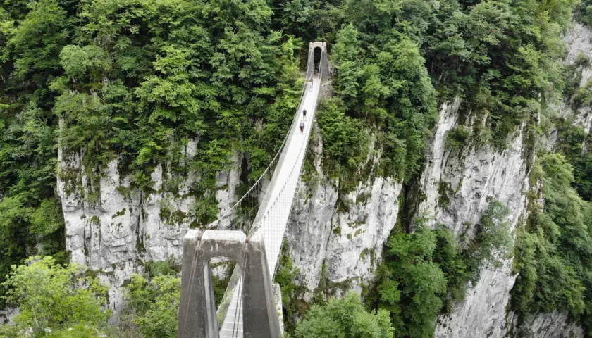 La pasarela de Holzarte cruza un profundo cañón verde, con personas caminando sobre ella.