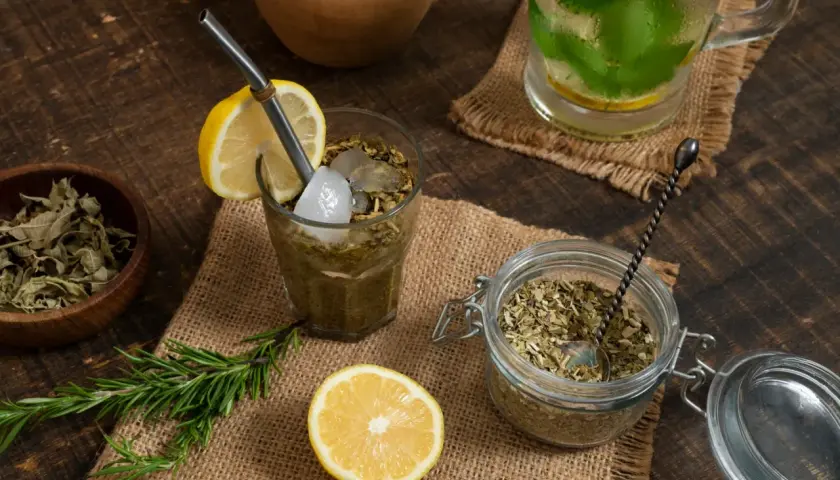 Orzeźwiająca yerba mate cytrynowa z lodem i rozmarynem, obok słoik z suszem i cytryna.