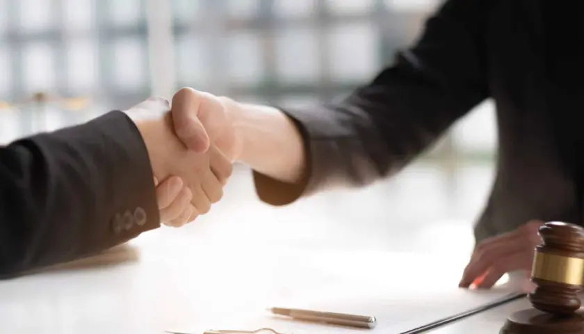 Poignée de main entre deux avocats, symbolisant un accord ou un **départage prudhomme**. Un maillet de juge est visible sur la table.