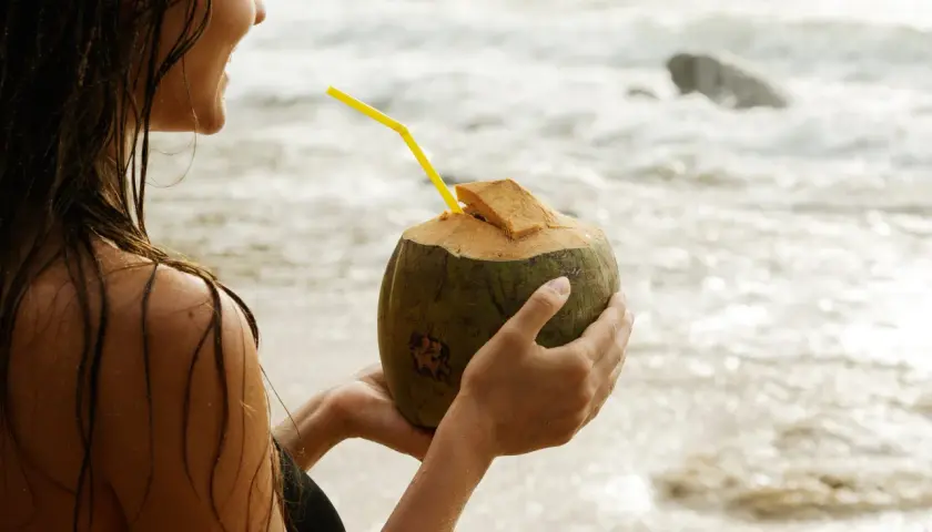 Kobieta na plaży pije wodę kokosową, doceniając jej orzeźwiające właściwości.