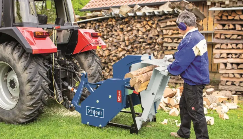 Mann bedient eine gebrauchte Scheppach Rolltischkreissäge mit Zapfwellenantrieb, bereit zum Holzhacken neben einem Traktor.
