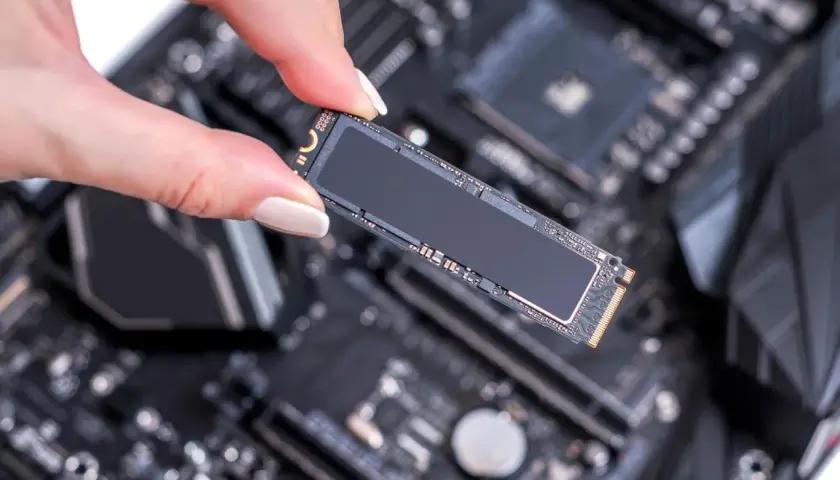 Eine Hand hält eine M.2 SSD, bereit für den Einbau in einen SSD-Steckplatz auf einem Computer-Motherboard.