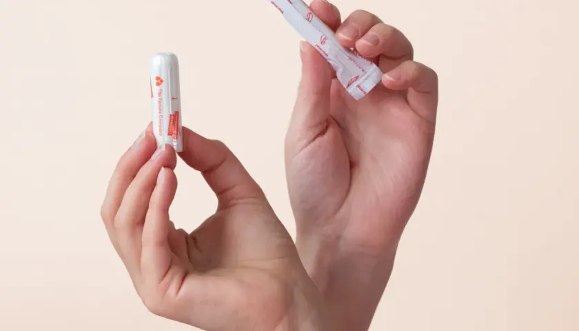 Zwei Hände halten Tampons. Einer ist ausgepackt, der andere noch in seiner Hülle. So sieht ein Tampon aus.