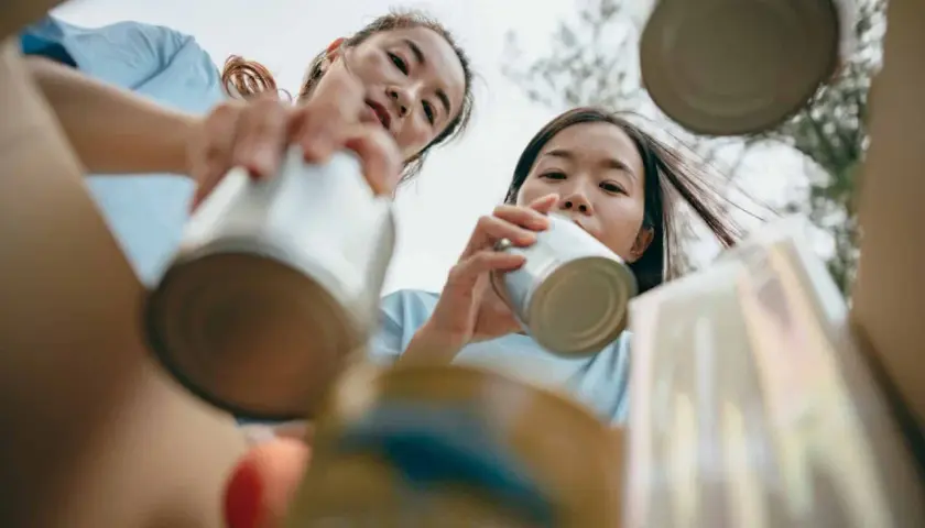 Two young women participate in voluntary community service, sorting cans for recycling.