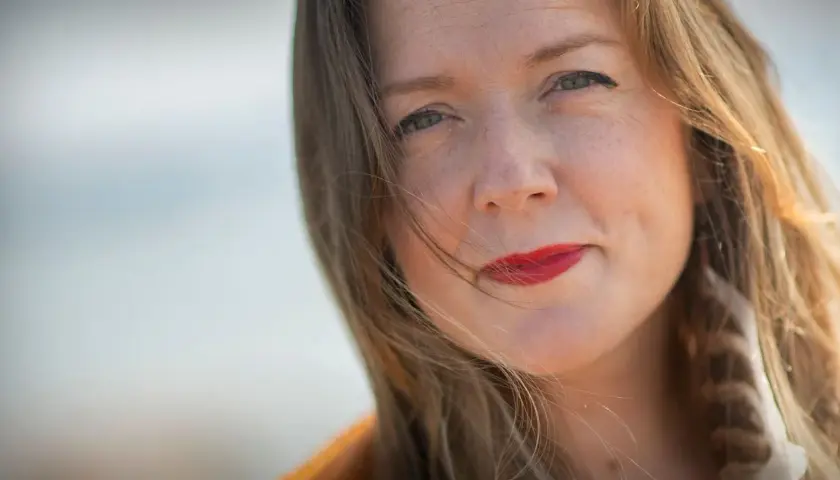 Tove Folkesson med rött läppstift och en fjäder i håret, fångad i ett mjukt ljus.