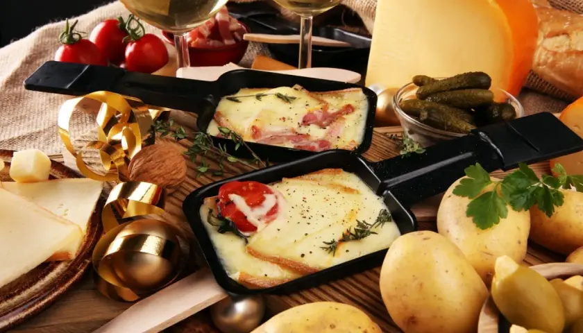 Comment présenter une raclette : fromage fondu, pommes de terre, cornichons et charcuterie, le tout prêt à être dégusté.