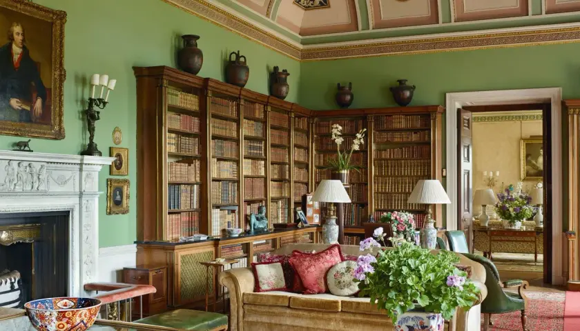 A cozy library with floor-to-ceiling bookshelves, a fireplace, and plush seating, embodying a classic countryside style.