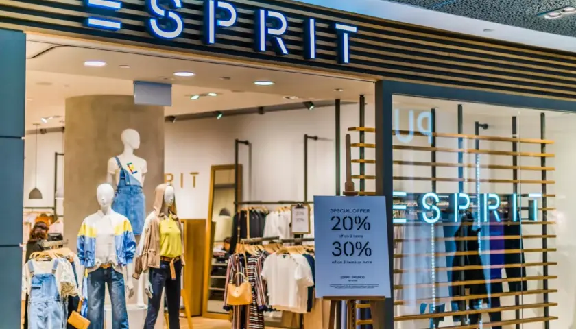 Sklep Esprit z neonowym logo. Manekiny prezentują letnie ubrania, a obok widoczna jest tablica z promocją.